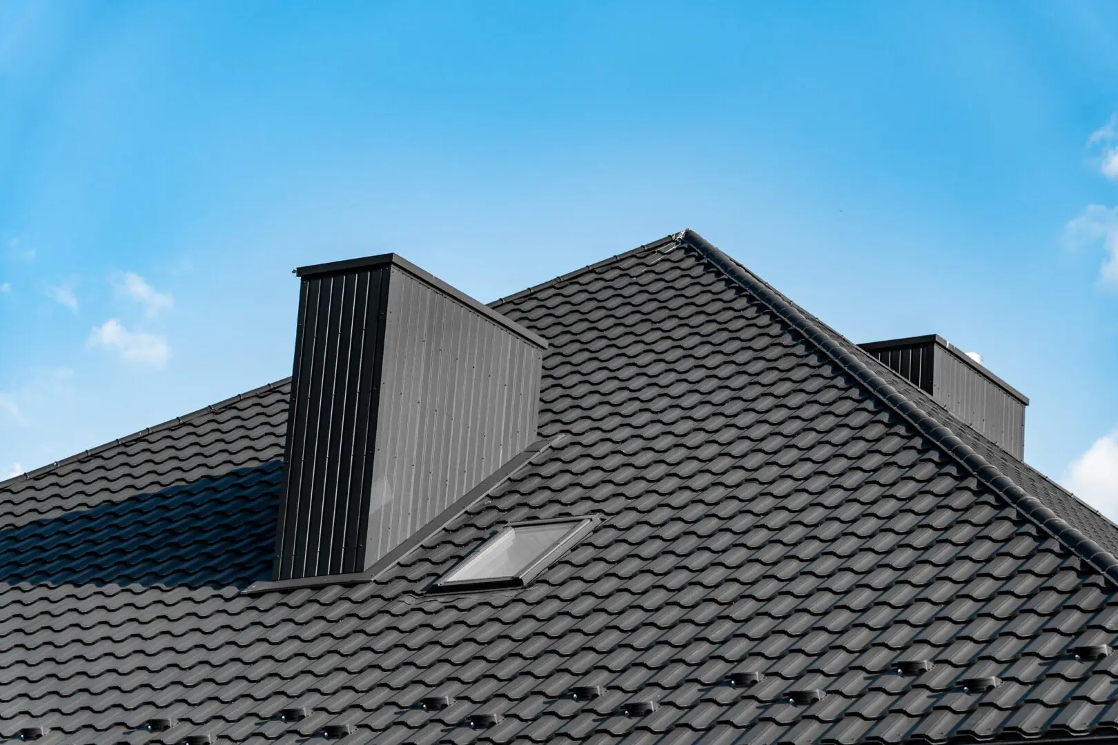 Modern black tiled roof against blue sky.